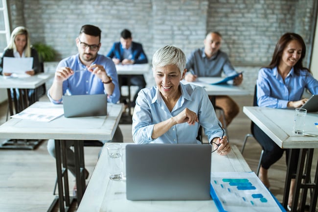 The image shows a modern classroom environment In the center a female student with glasses looking at a laptop The girl is 17 studying for her Alevels so has some revision textbooks to her side The titles are not redable She is in a UK classroom an s